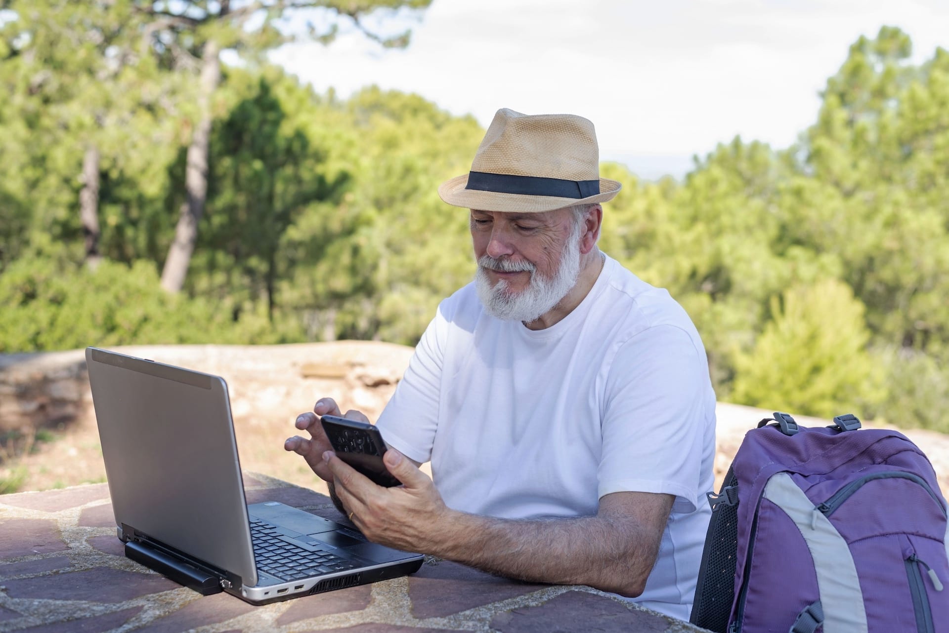 Older man using laptop outdoors with mobile, representing wireless internet solutions and business fibre internet access